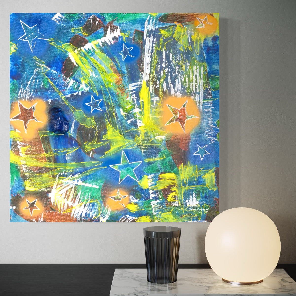 a multi-coloured original canvas painting styled on a shadowed wall above a table with a round lamp and glass on it
