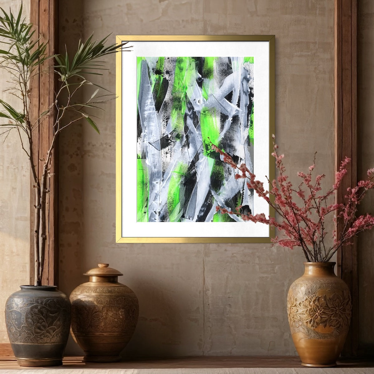 A green abstract paper art print in an antque gold frame styled on a neutral wall surrounded by big plant pots