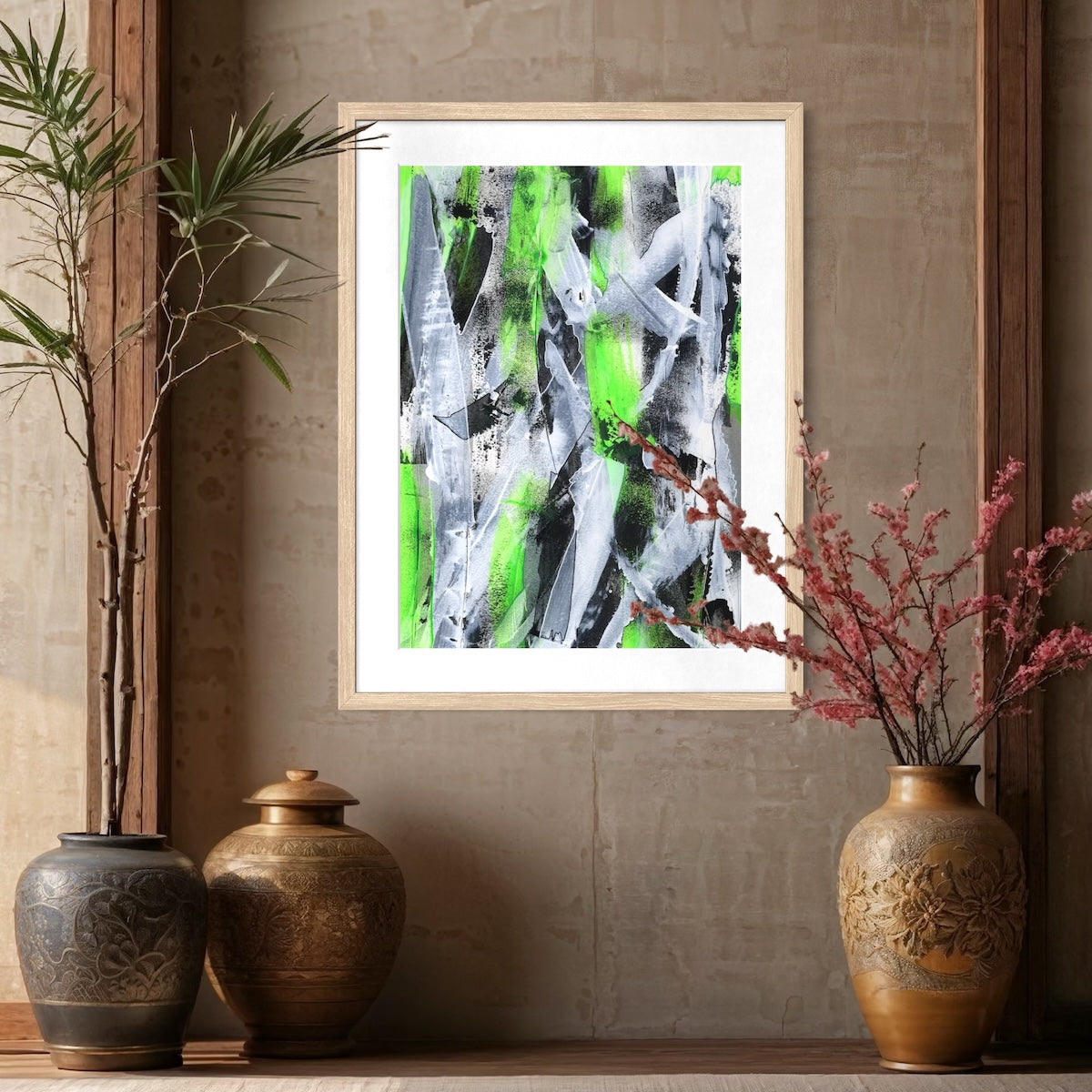 A green abstract paper art print in a natural frame styled on a neutral wall surrounded by big plant pots