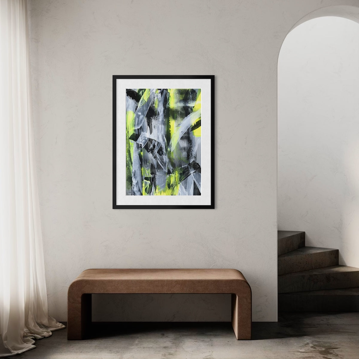 A yellow abstract paper art print in a black frame styled on a light wall in a hallway above a wooden bench next to a staircase