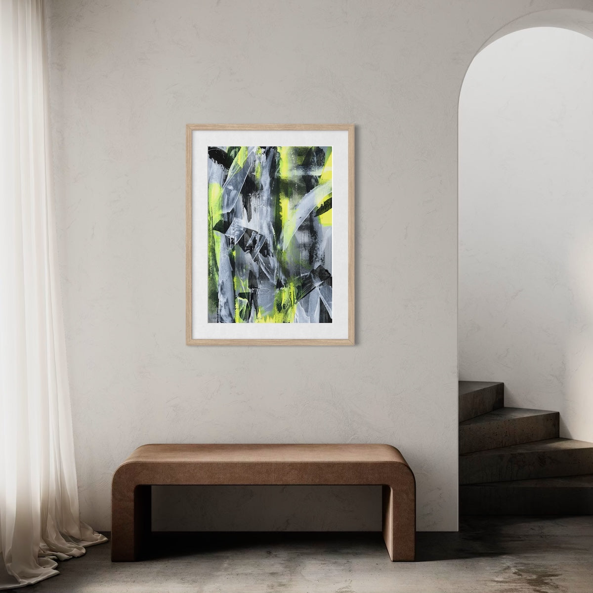 A yellow abstract paper art print in a natural frame styled on a light wall in a hallway above a wooden bench next to a staircase