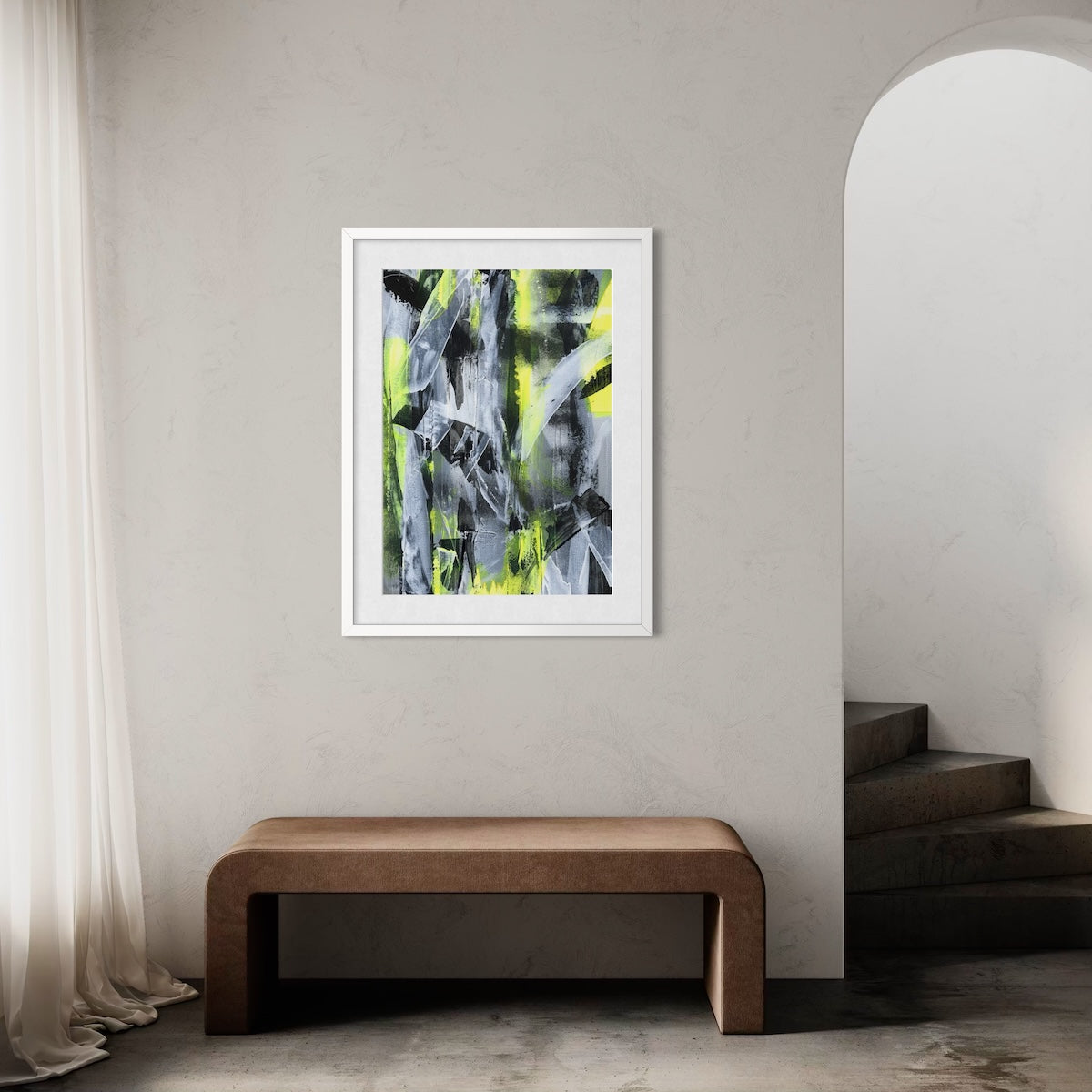 A yellow abstract paper art print in a white frame styled on a light wall in a hallway above a wooden bench next to a staircase