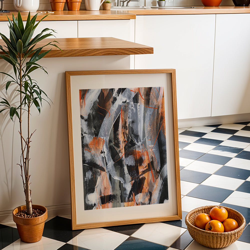 an orange original art abstract in a natural wood frame against a kitchen unit next to a plant and a bowl of fruit.