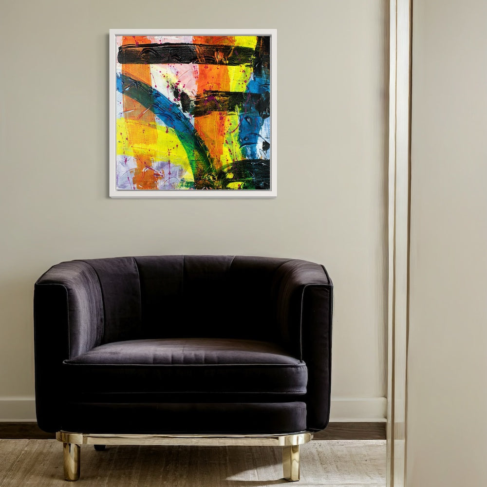 a multi-coloured abstract original canvas in a white frame styled on a light above a dark single sofa