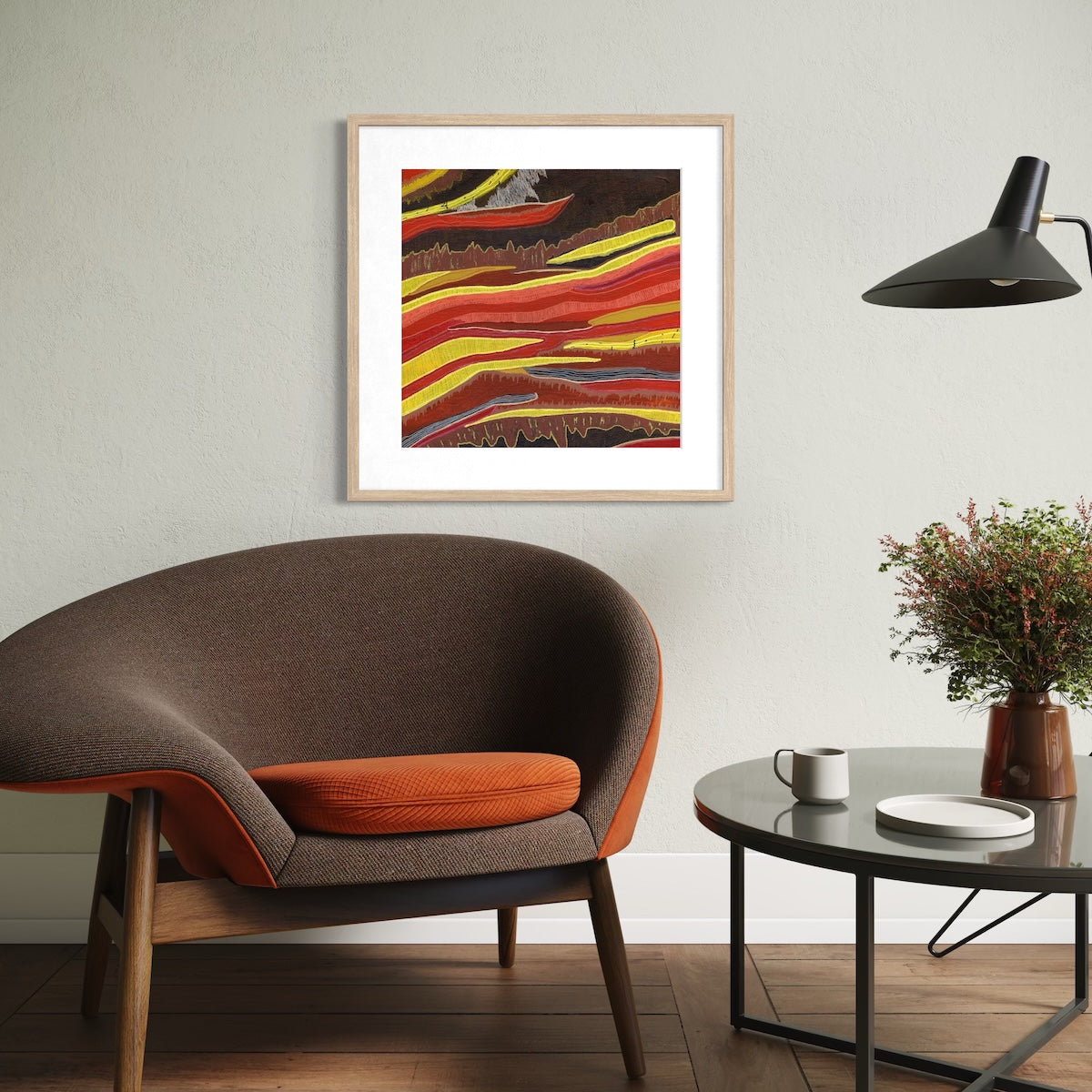 A multi-coloured paper art print in a natural frame styled on a light wall next to a table and chairs.