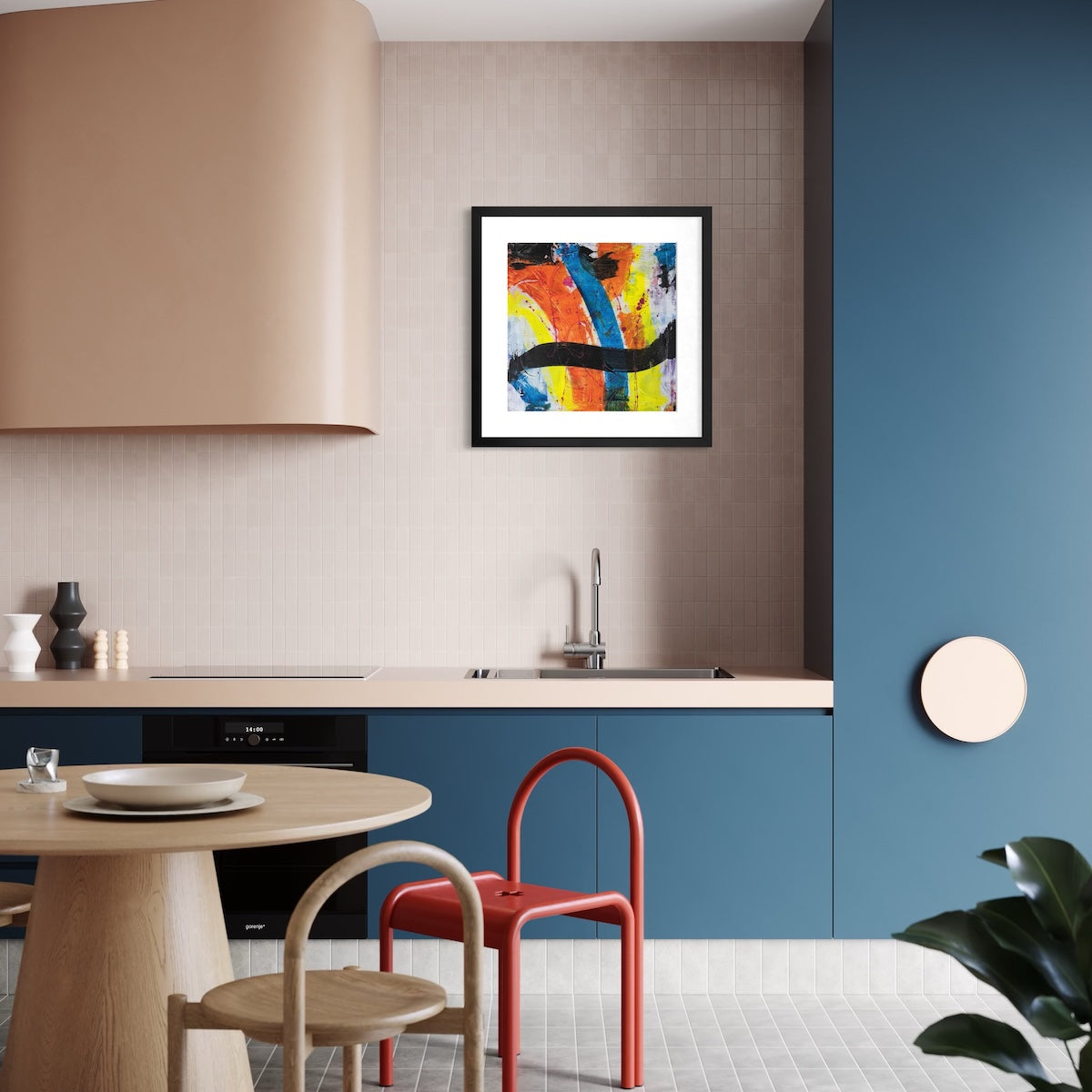 A colourful paper art print in a black frame styled on a light wall in a kitchen with blue cupboards.