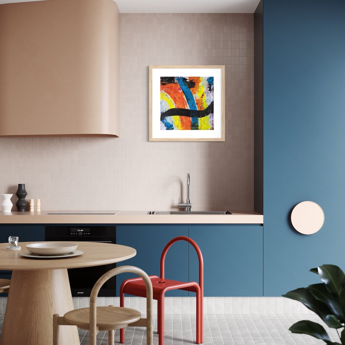 A colourful paper art print in a natural frame styled on a light wall in a kitchen with blue cupboards.