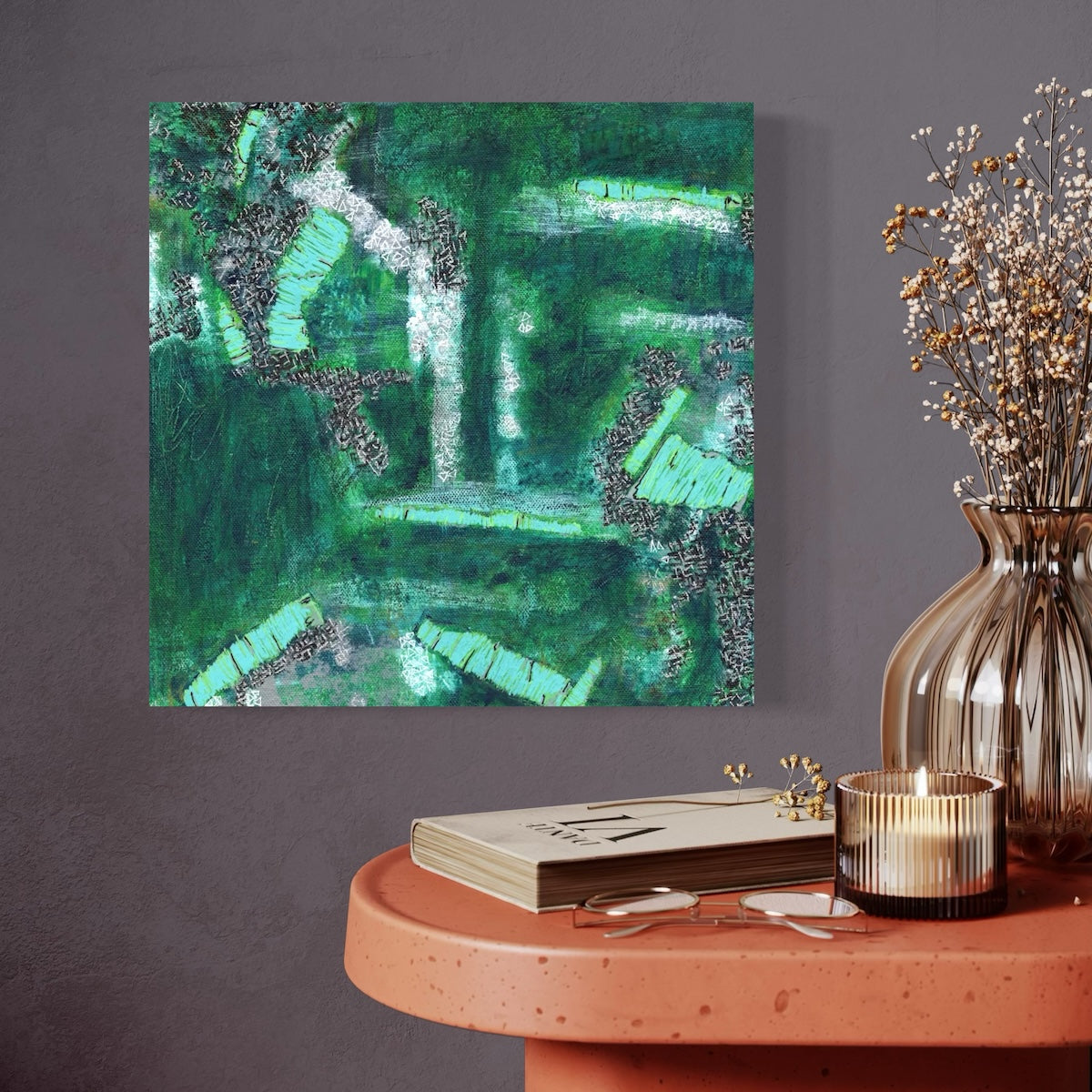 A green abstract canvas original styled on a dark wall next to an orange table with a candle and a vase.