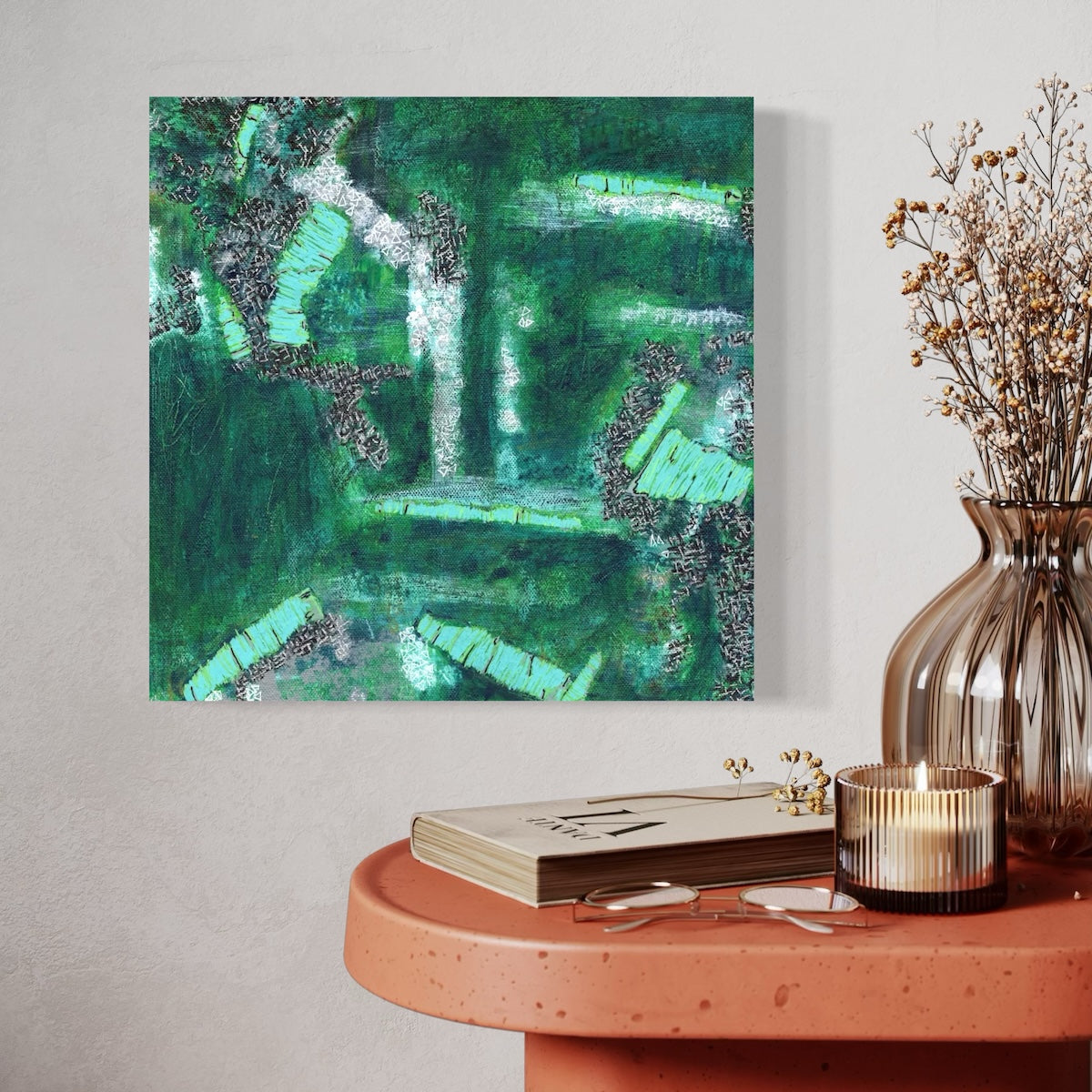 A green abstract canvas original styled on a light wall next to an orange table with a candle and a vase.