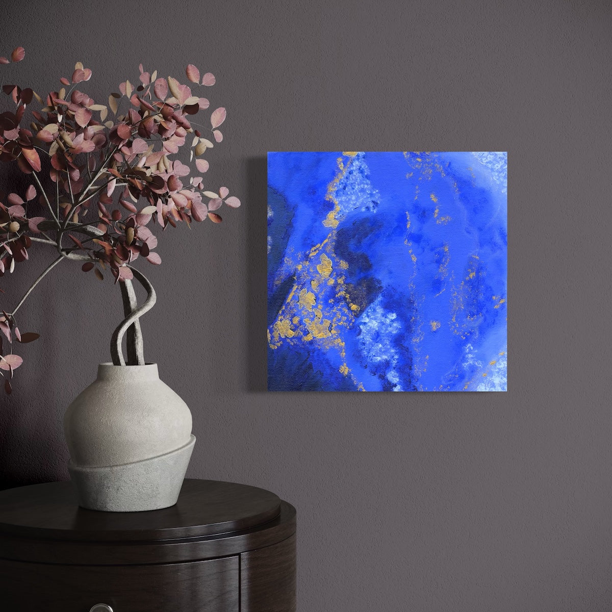 a blue abstract original canvas on a dark wall next to a vase of flowers