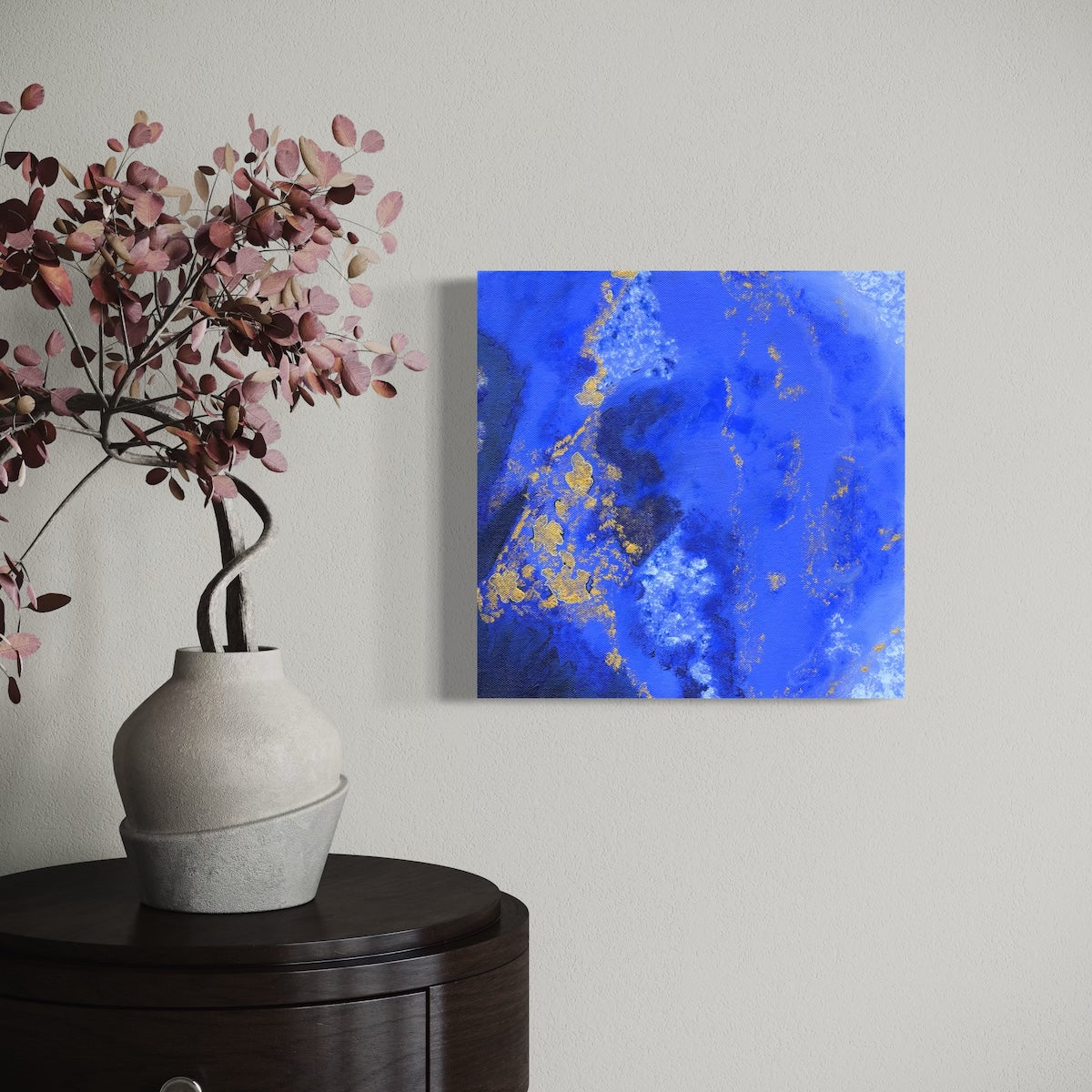 a blue abstract original canvas on a light wall next to  vase of flowers
